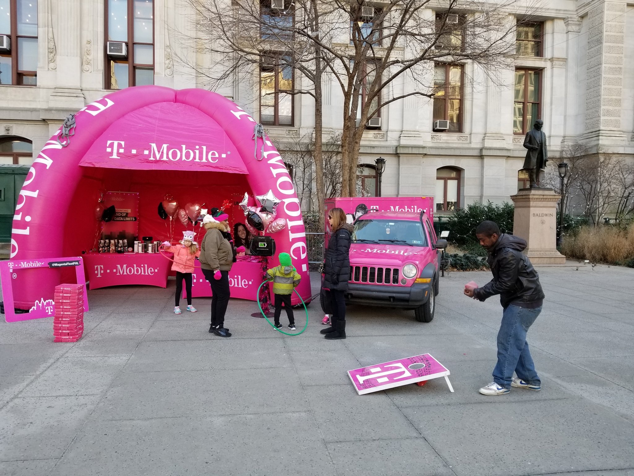 Families play games beside a magenta T-Mobile tent and mobile vehicle at an outdoor community activation